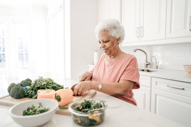 An old woman cutting vegetables in the kitchen.